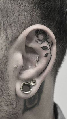 a man with tattoos on his ear and behind the ear is a cross, leaves and a flower