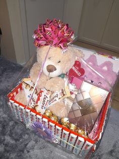 a teddy bear in a gift box with chocolates and candies on the floor