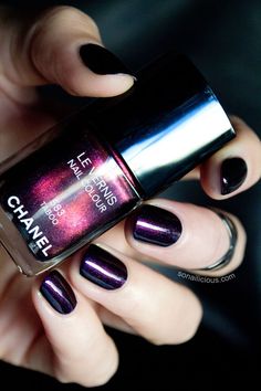 a person holding onto a purple and black nail polish with metallic flakes on it