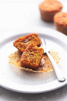 two muffins on a plate with a fork and cupcake in the background