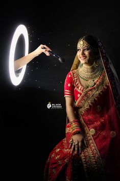 a woman in a red and gold bridal outfit is holding a light up ring