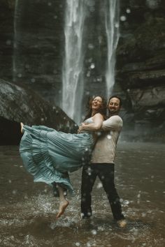 a man and woman standing in front of a waterfall holding each other with their arms