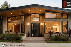 a modern style house with lots of windows and plants in the front yard at dusk