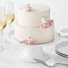 there is a white cake with pink flowers on it and two wine glasses next to it