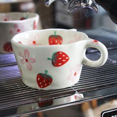 two cups with strawberries painted on them are sitting on a coffee maker's shelf