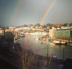 a rainbow in the sky over a river with buildings and boats on it's bank