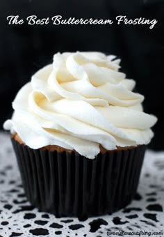 a cupcake with white frosting on a doily next to a black and white napkin