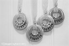 three silver pendants with words on them hanging from a white ribbon in black and white