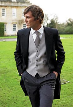 a man wearing a suit and tie walking in front of a large building with grass