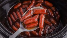 a spoon full of cooked hot dogs in a crock pot with sauce on top