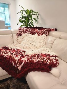 a white couch with a red and white blanket on it next to a potted plant