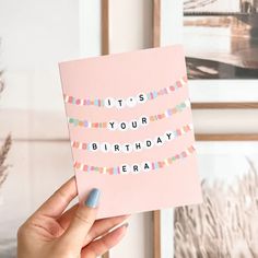 someone holding up a pink birthday card with the words it's your birthday on it