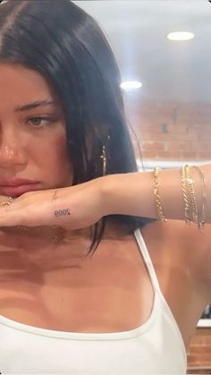 a woman with tattoos on her arm posing for the camera in a kitchen, wearing gold bracelets and a white tank top