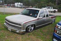 a silver truck parked on top of a grass covered field next to other cars and trucks