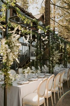 an outdoor dining area with tables, chairs and white flowers on the tablecloths