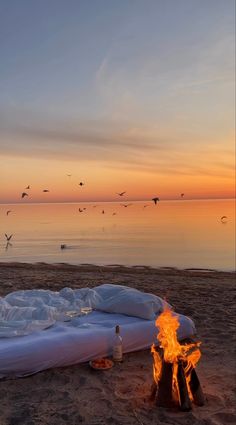 a fire pit sitting on top of a sandy beach next to the ocean at sunset