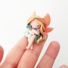 a tiny doll sitting on top of a persons finger in front of a white background