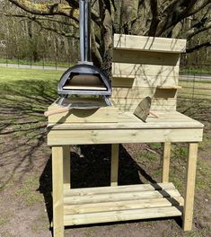 a wood stove sitting on top of a wooden table next to a tree and grass field