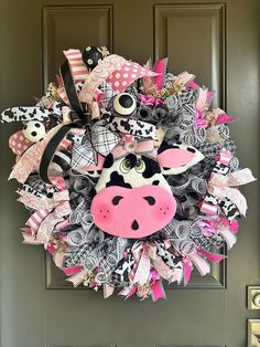 a cow wreath is hanging on a door with pink, black and white ribbons around it