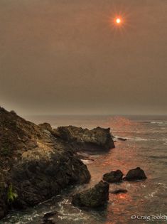 the sun is setting over the ocean and rocks