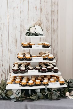 a tiered cake with cupcakes and flowers on the top is decorated with greenery