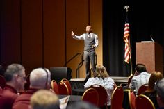 a man giving a speech to an audience in front of a podium with american flags