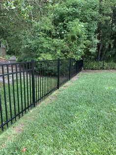 a black metal fence in the middle of a grassy area with trees and bushes behind it