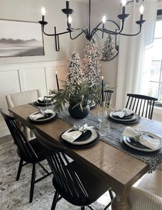 a dining room table is set with black and white plates, place settings and candles