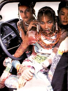 three women sitting in the drivers seat of a car, one with tattoos on her arm