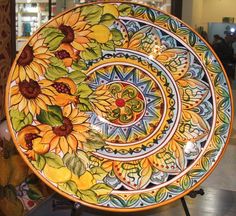 a plate with sunflowers painted on it is sitting on a stand in a store