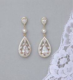 two pairs of earrings with pearls hanging from the end of each earring, on top of a lace doily