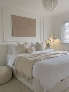 a white bedroom with a chandelier hanging from the ceiling and pillows on the bed