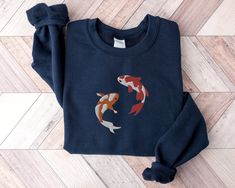 Dive into an ocean of style with our Embroidered Japanese Koi Fish Sweatshirt, a unique fusion of Japanese artistry and marine motifs. This sweatshirt features an intricately embroidered koi fish, symbolizing perseverance and good fortune, surrounded by elements of the deep sea, including majestic whales and powerful sharks. The Japanese-inspired design creates a harmonious blend of cultural richness and marine aesthetics, making it a standout piece for those who appreciate art and the wonders of the ocean. Crafted for both comfort and style, this sweatshirt is the perfect choice for expressing your love for Japanese art, marine life, and unique fashion. Make a splash with our Japanese Koi Fish Sweatshirt - a symbol of strength and elegance that adds a touch of art and adventure to your wa Koi Fish Shirt, Crewneck Style, Nurse Sweatshirt, Embroidered Sweatshirts, Fishing Shirts, Koi Fish, Nurse Gifts, Unisex Design, Koi