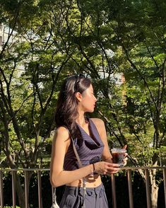 a woman standing in front of trees holding a drink