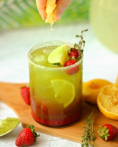 a person is holding a lemon wedge over a drink with strawberries and limes