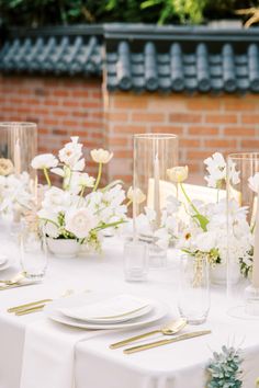 the table is set with white flowers and gold place settings