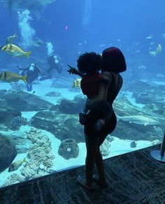 a woman holding a child in her arms looking at fish and other marine life inside an aquarium