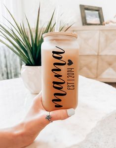 a person holding up a mason jar with the word boooo on it and a plant in the background