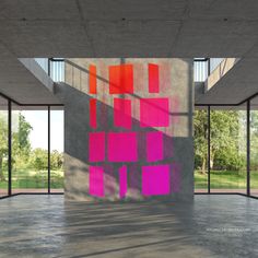 an empty room with pink and red squares on the wall, in front of large windows