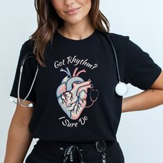 Order by DECMBER 6TH to ensure Christmas delivery. Delivery dates are not guaranteed.  To ensure adequate time for production and shipping, orders must be placed NO LATER THAN DECEMBER 6TH. Show off your cardiac pride with our CVICU Cardiac Nurse Heart Shirt. This shirt features a retro-style heart anatomy with a stethoscope and the funny phrase "Got Rhythm? I Sure Do," this is perfect for cardiology students, cath lab RNs, and the cardiologist crew. It's also a great funny heart anatomy shirt f Nurse Tshirt, Cardiac Technologist, Cardiac Cath Lab Nurse, Black Nursing Top With Graphic Print, Ekg Technician Shirts, Cardiac Shirt Design, Black Graphic Print Nursing Top, Cath Lab Nurse, Heart Beat T Shirt