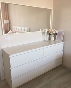 a white dresser sitting next to a mirror and vase with flowers on top of it