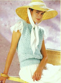 a woman in a straw hat sitting on a wicker chair wearing a blue sweater and white scarf