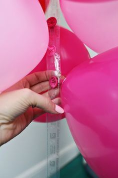 a person is holding pink balloons and measuring them with a tape to measure the balloon