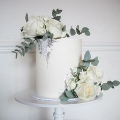 a white wedding cake with flowers and greenery on the top tier, sitting on a stand