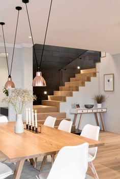 a dining room table with candles and flowers on it in front of stairs that lead up to the second floor