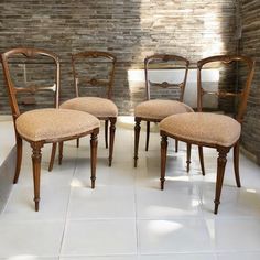 four wooden chairs sitting next to each other on a tile floor in front of a brick wall