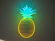 a neon sign with a pineapple on it's side hanging from the wall