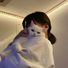 a woman holding a white cat in her arms with lights on the wall behind her