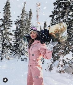 a woman standing in the snow with skis on her head and holding a board