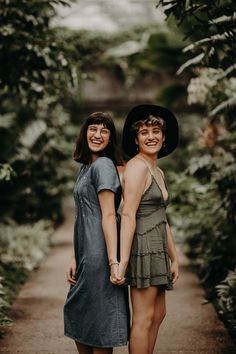 two women standing next to each other on a dirt path in the woods holding hands